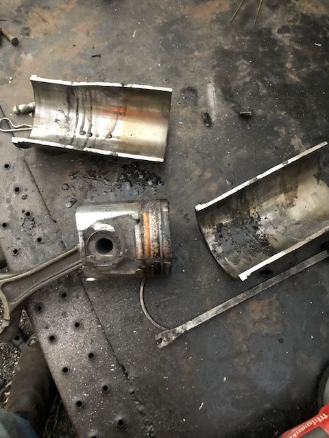 Damaged engine piston and cylinder parts on a dark metal surface.