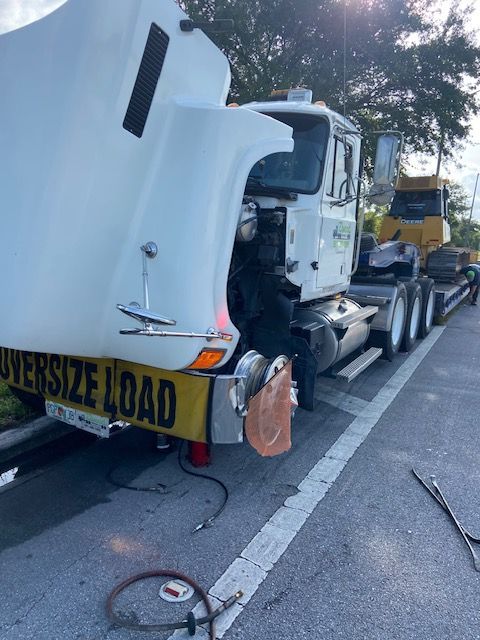 White semi-truck with open hood; carries yellow bulldozer on a flatbed trailer.