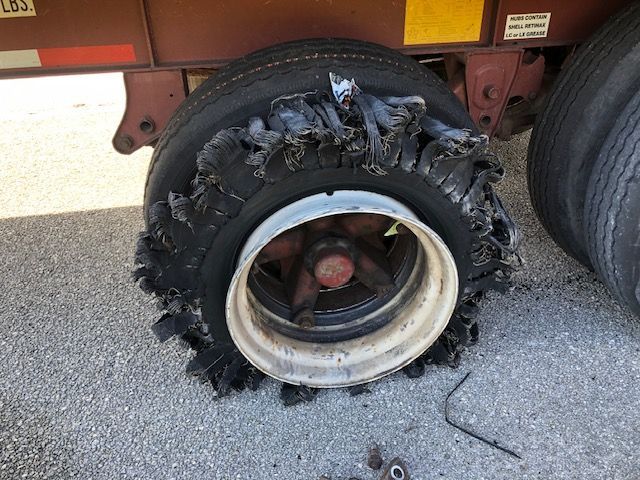 Damaged semi-truck tire; sidewall shredded, rim exposed.