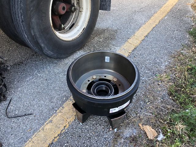Semi-truck tire with removed brake drum, on asphalt with yellow lines.