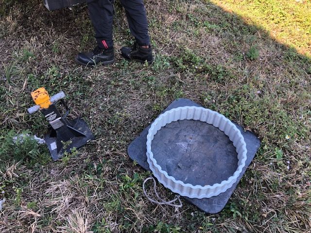 Person standing near black stand with yellow tool, and gray circular frame on black pad, grass setting.
