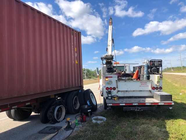 A semi-truck with a cargo container being assisted by a white service truck on a roadside.