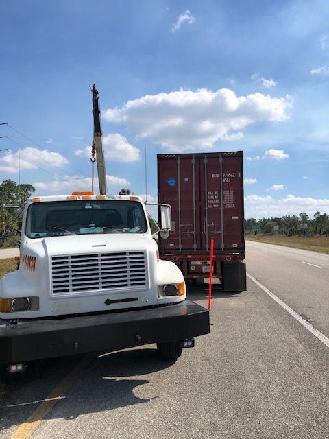 A tow truck and a cargo container on a roadside under a blue sky.