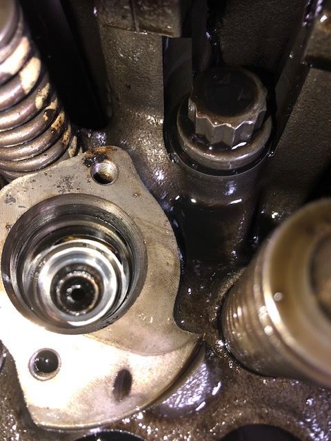 Close-up of an engine component with oil. A valve, bolt, and spring are visible.