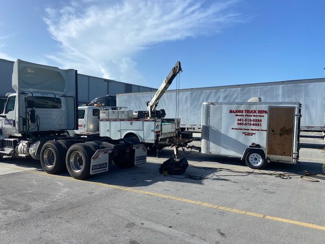Truck and trailer being worked on outdoors with a crane, sunny day.
