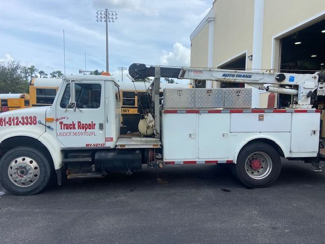 White service truck with crane and storage boxes parked outside a building.
