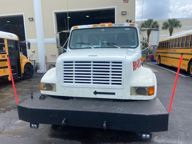 White truck with flatbed, parked near yellow school buses.