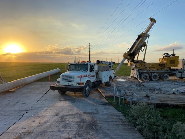 White truck and drilling rig working near power lines at sunset.