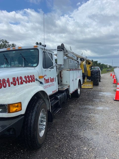 White utility truck on a road, arm extended toward the side, safety cones present.