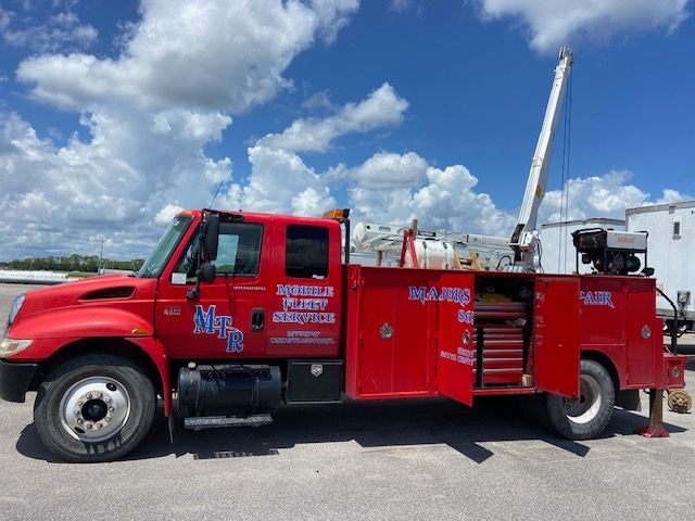 Red service truck with crane and open toolbox in front of a blue sky.