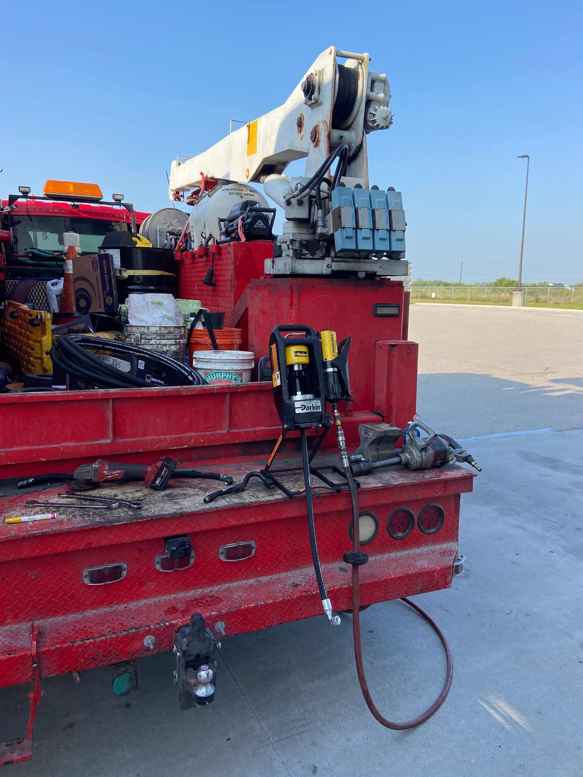 Red utility truck with crane boom extended, tools on the flatbed, under a blue sky.