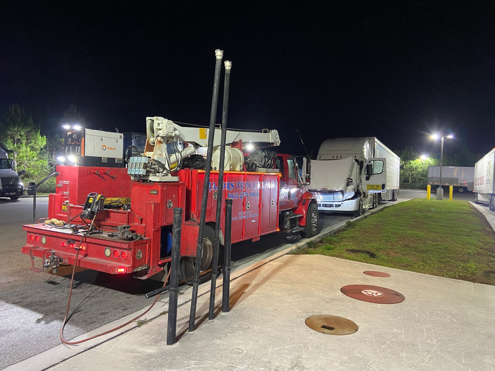 Red service truck parked at night, servicing a semi-truck with lights illuminating the scene.