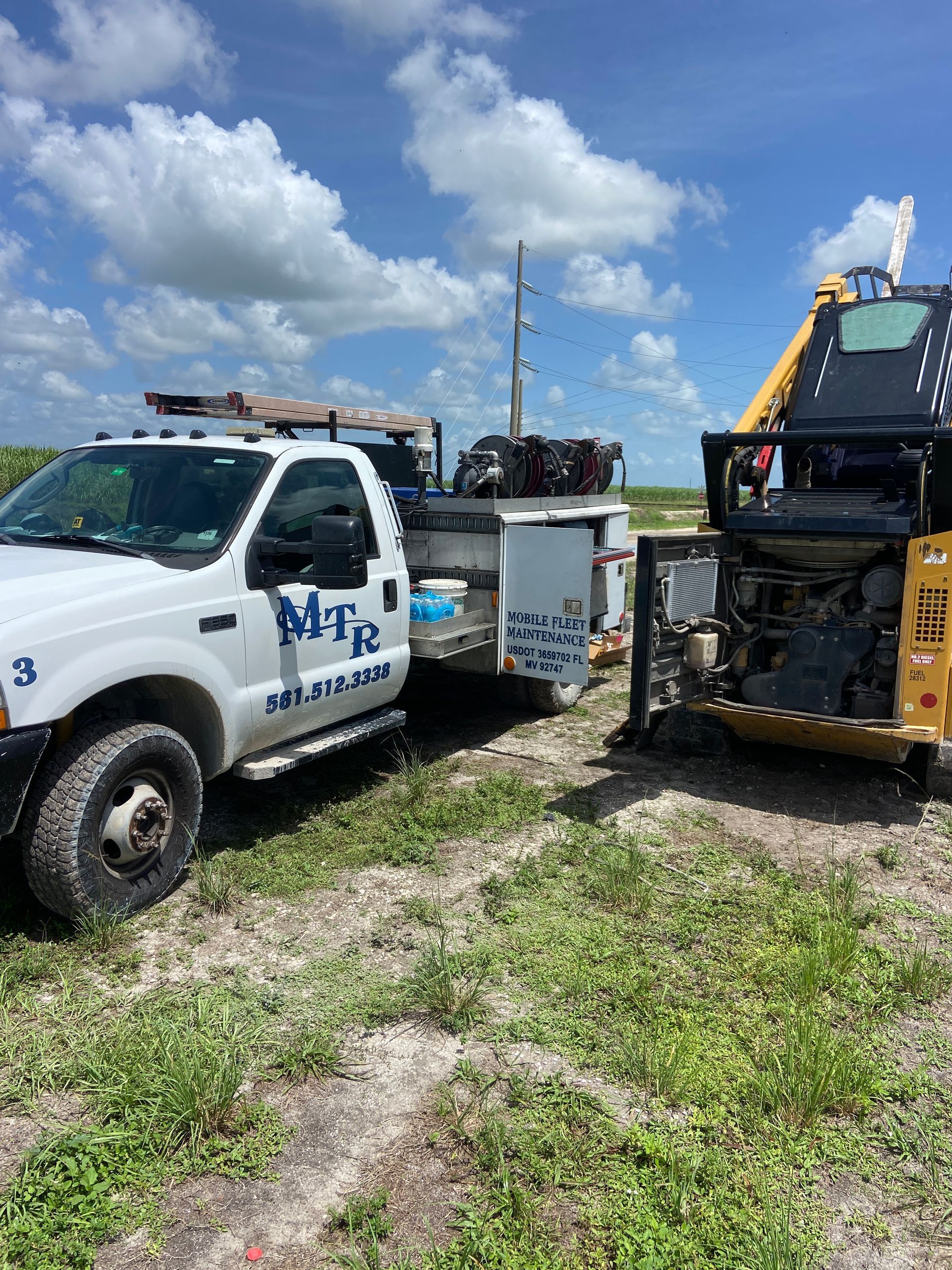 White MTR tow truck pulling yellow construction equipment in field under cloudy sky.