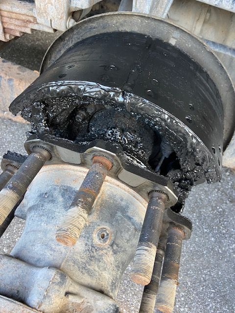 Damaged truck brake component, melted black rubber and metal, bolts visible.