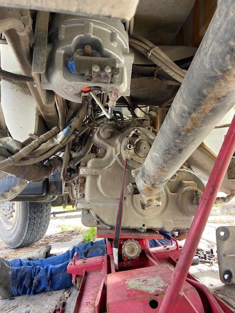 Mechanic under a truck, working on the drivetrain with a jack.