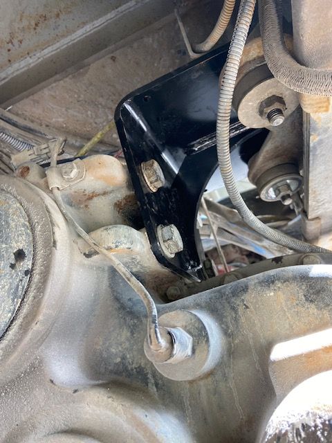 Black metal bracket bolted to a vehicle's underside, near a suspension component.