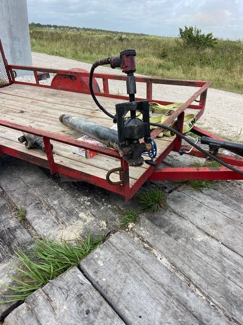 A red trailer with equipment, including a pump, on a wooden deck in a grassy area.