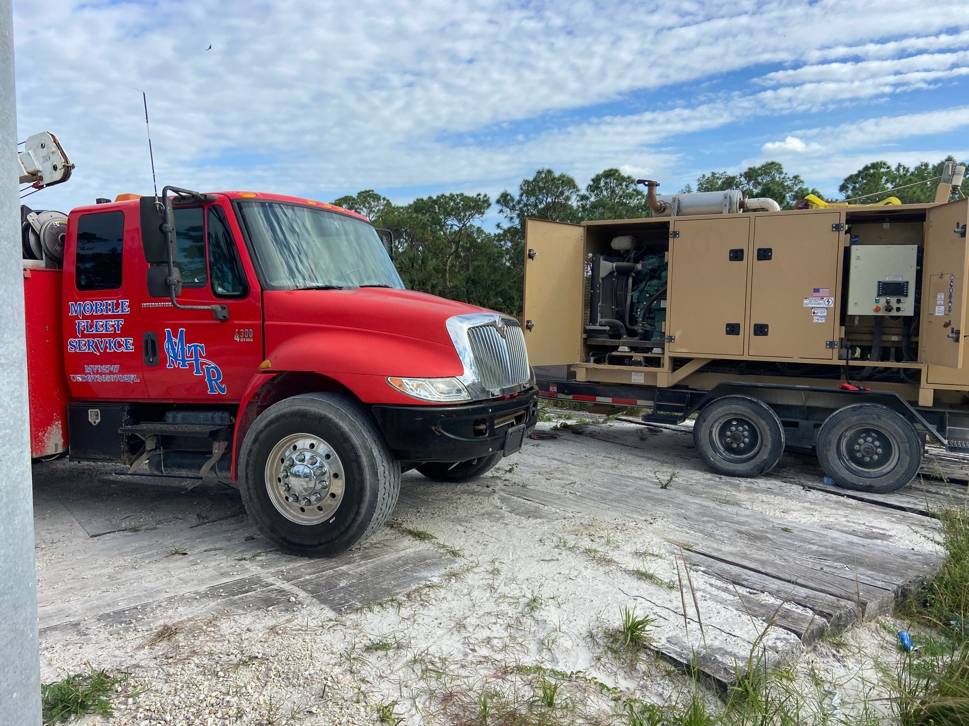Red truck towing a beige generator on a wooden surface outdoors, under a blue cloudy sky.