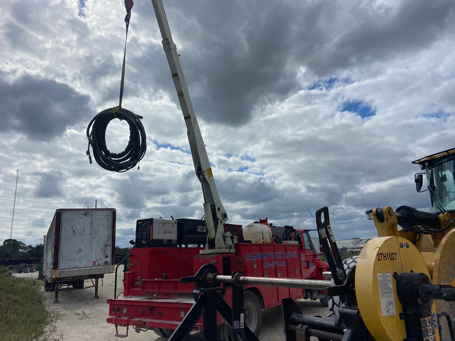 A crane lifts a coiled black cable from a red truck, with a cloudy sky background.