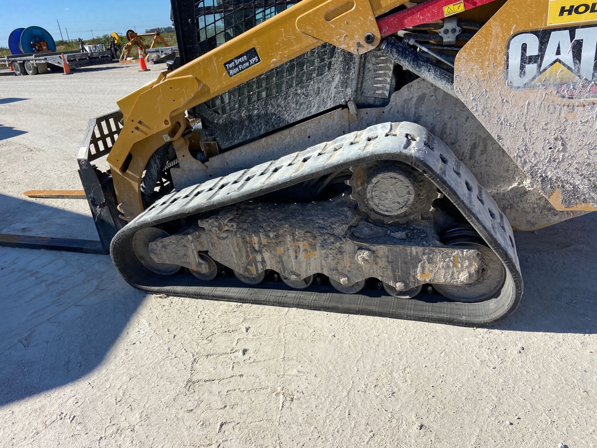 Yellow Caterpillar skid steer track on concrete, covered in mud.