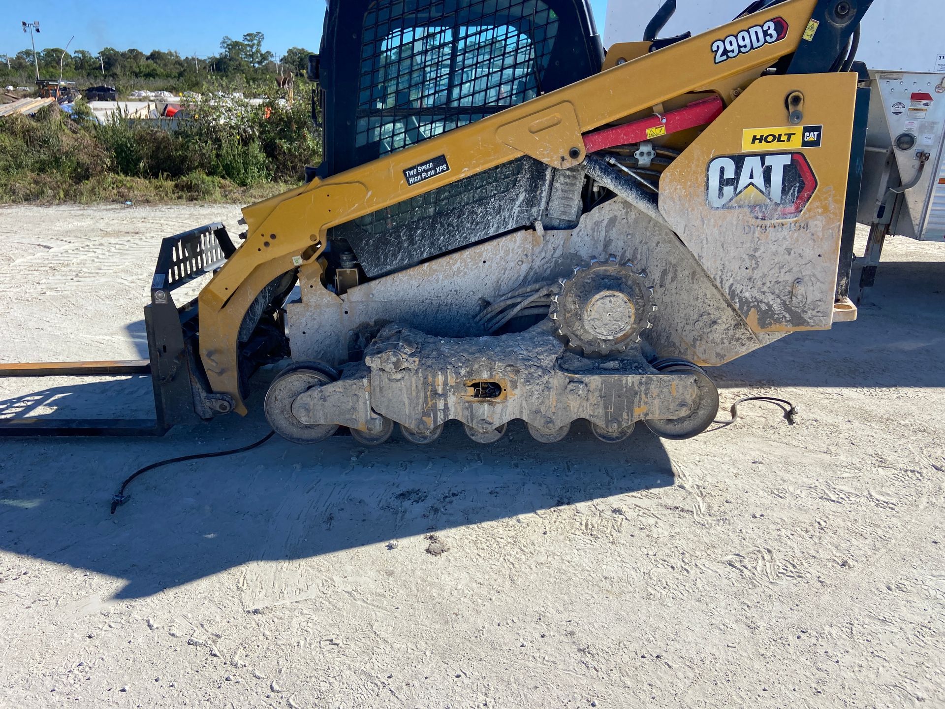 Yellow and black CAT skid steer on tracks, covered in dirt, parked on a gravel surface.