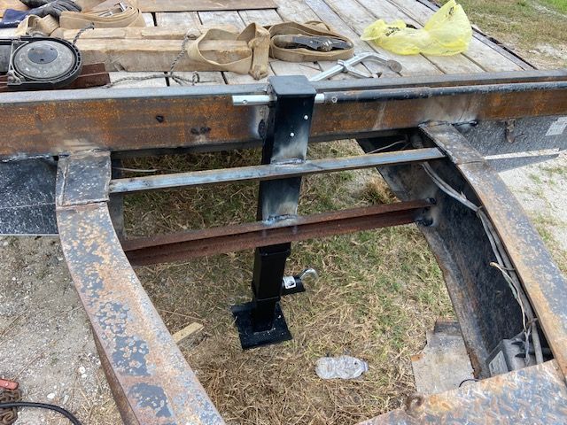 Welded trailer jack assembly on a rusty trailer frame, outdoors.