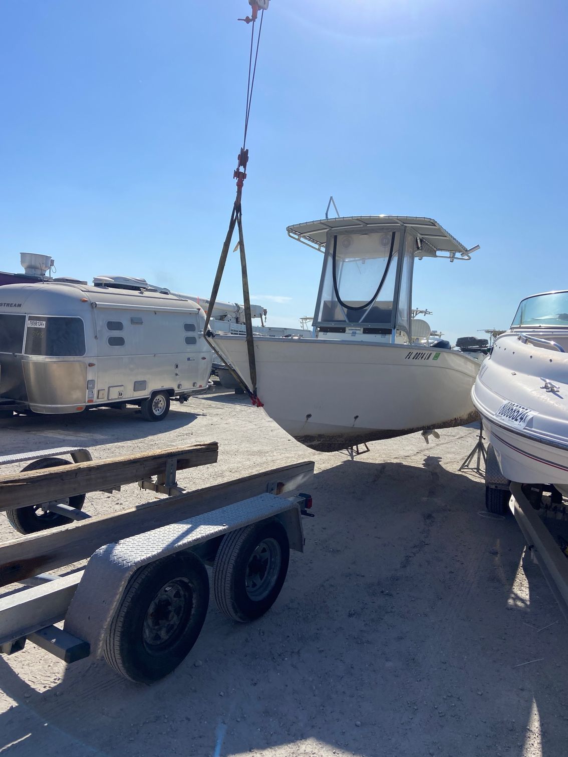 A boat suspended by a crane over a trailer in a sunny outdoor setting.
