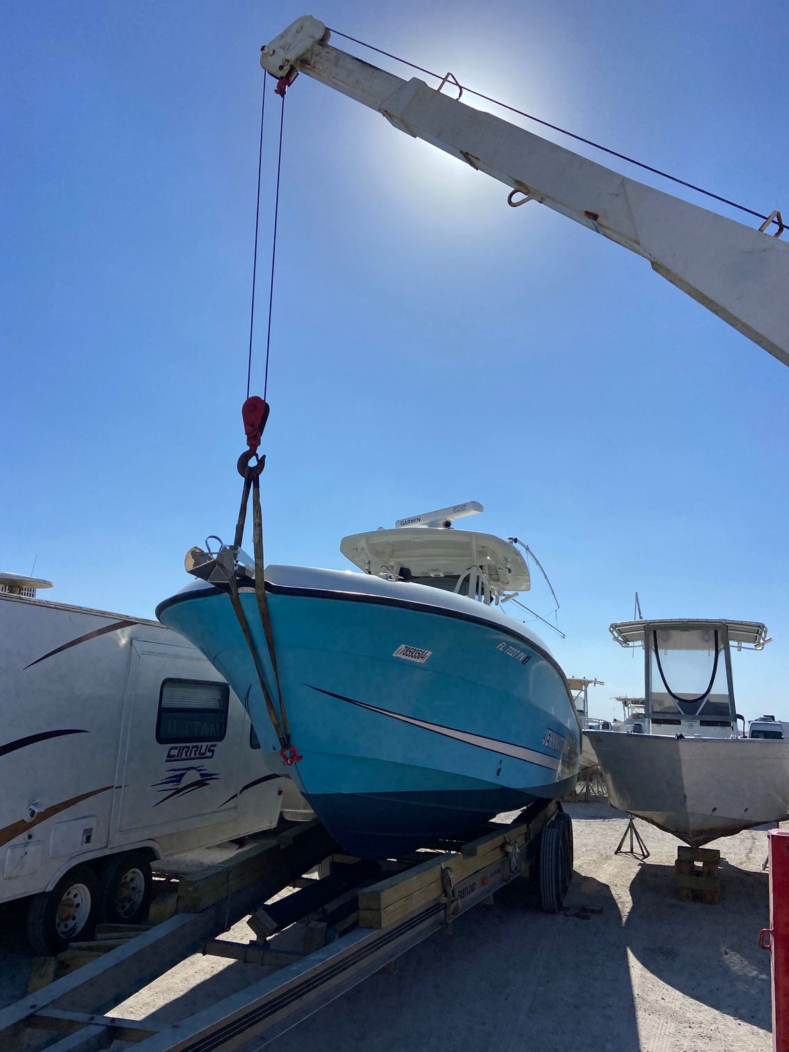 A turquoise boat suspended by a crane, over a trailer, outdoors on a sunny day.