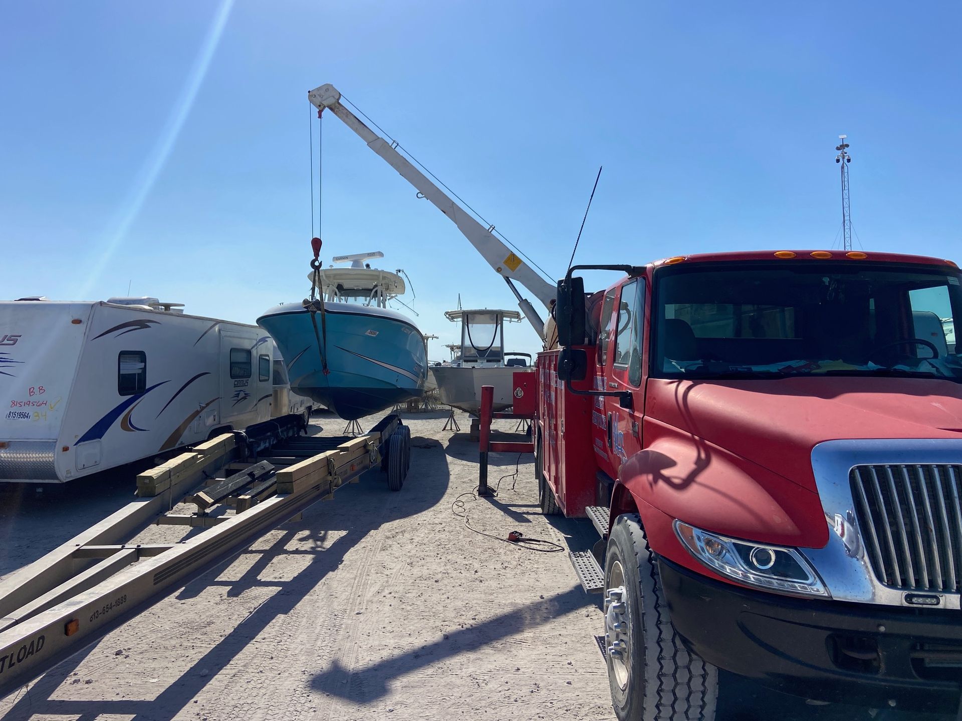 Red tow truck lifting a blue boat onto a trailer on a bright day.
