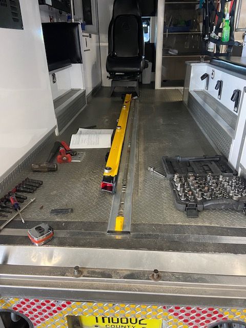 Inside of an ambulance. Tools and a yellow track are on the floor. A chair is visible at the back.