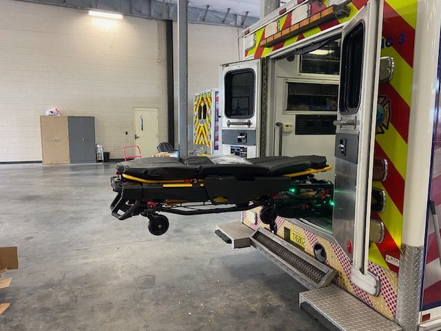 Ambulance with open doors; stretcher extended out. Interior of a garage.