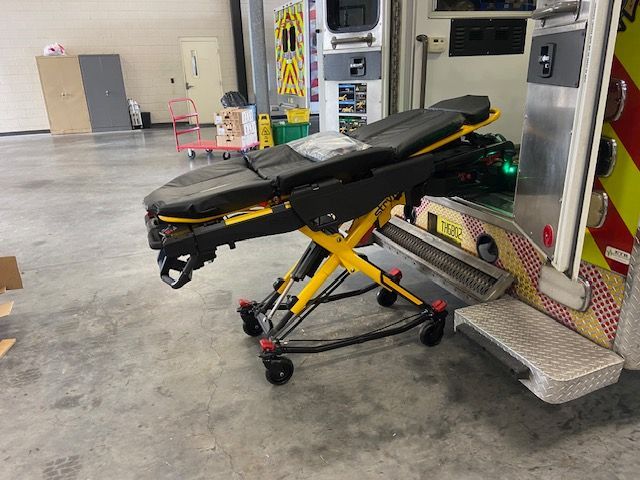 Ambulance stretcher on the ramp of an ambulance in a bay. Black and yellow frame, gray floor.