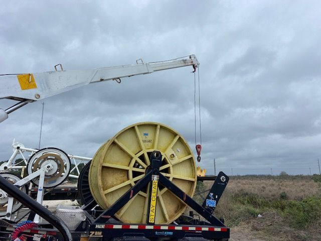 Crane lifting a large yellow spool of cable on a truck bed, under a cloudy sky.