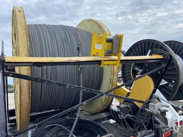 Large spool of gray cable mounted on a yellow and black metal cable reel trailer.