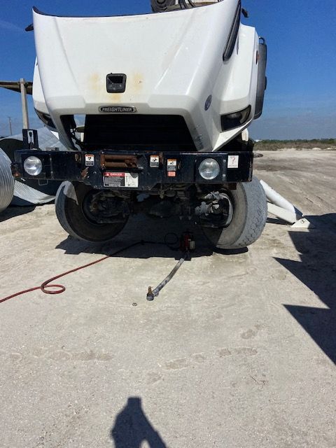 White truck with open hood, tire lifted by jack, red hose on ground.