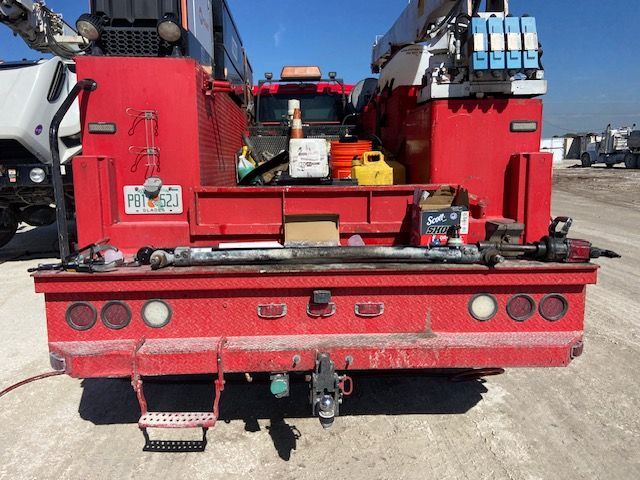 Red truck bed with equipment, tools, and a long silver driveshaft on the bed.