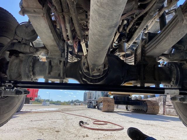 Underside of a heavy-duty truck chassis. Differential, driveshaft, and suspension components are visible in a work yard.