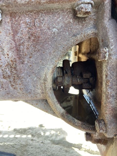 Rusty tractor axle with a bolted joint, possibly leaking fluid.