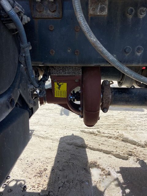 Undercarriage of a truck with a brown differential, driveshaft, and various components against a light-colored surface.