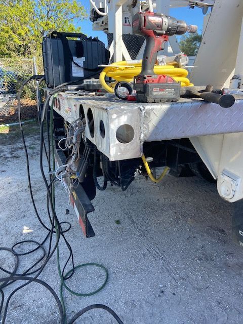 Rear of a tow truck with tools on the platform, including a drill and coiled yellow cable.
