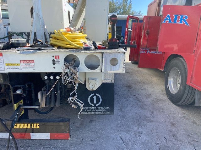 Rear of a white utility truck with exposed wires, next to a red truck, outdoors.