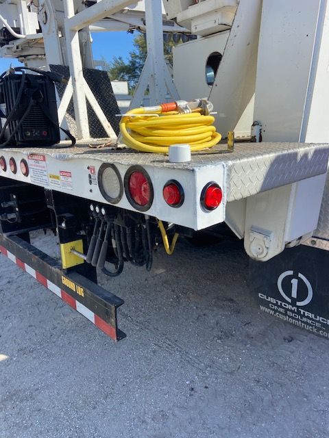 Rear of a white truck with red lights, a yellow hose, and a black bag on its flatbed.