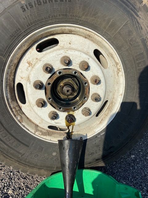 Truck wheel with oil leaking into a funnel, likely for a hub seal replacement.
