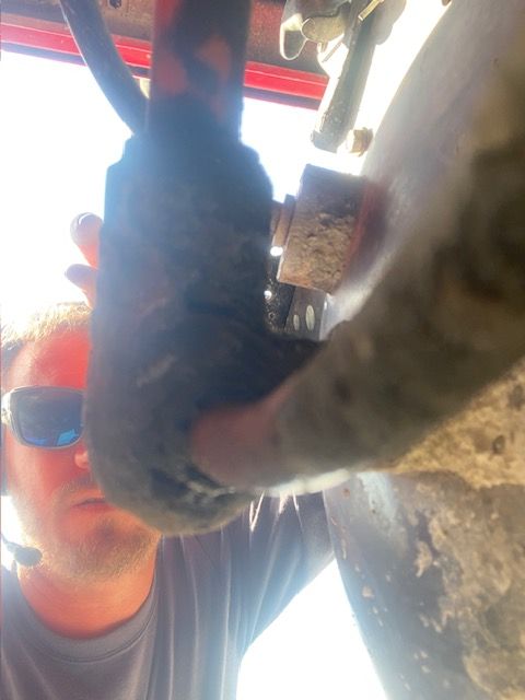 Man looking at vehicle suspension. Close-up view of the part with a bolt visible, outdoors.