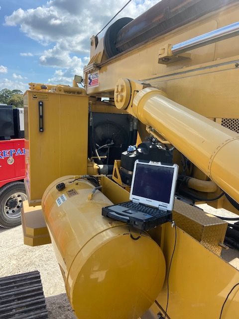 Yellow crane with a laptop on its fuel tank, likely for diagnostics or maintenance in an outdoor setting.