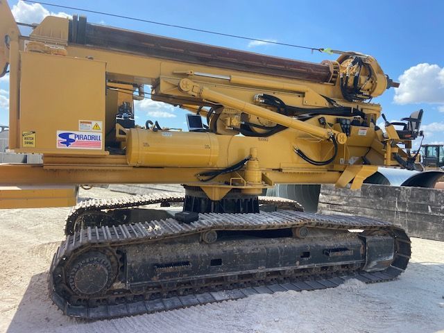 Yellow construction drill on tracks, outdoors.