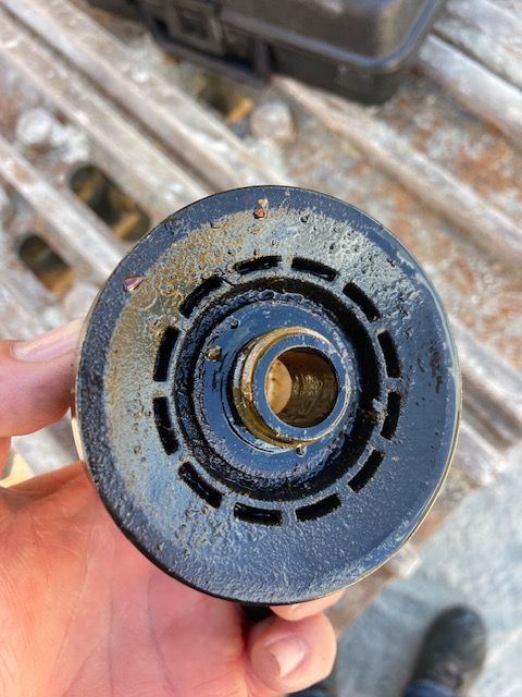 Black oil filter end held in hand, showing central hole and surrounding ridges, with oil residue.