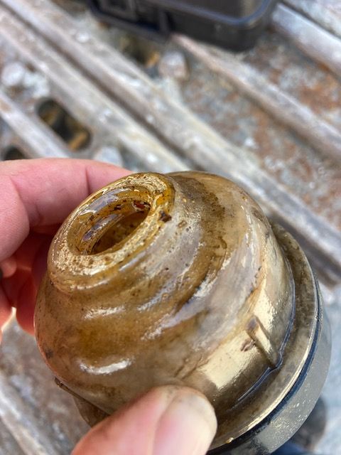 Close-up of a dirty, clear plastic fuel filter cup being held by a hand. Brown liquid is visible inside.