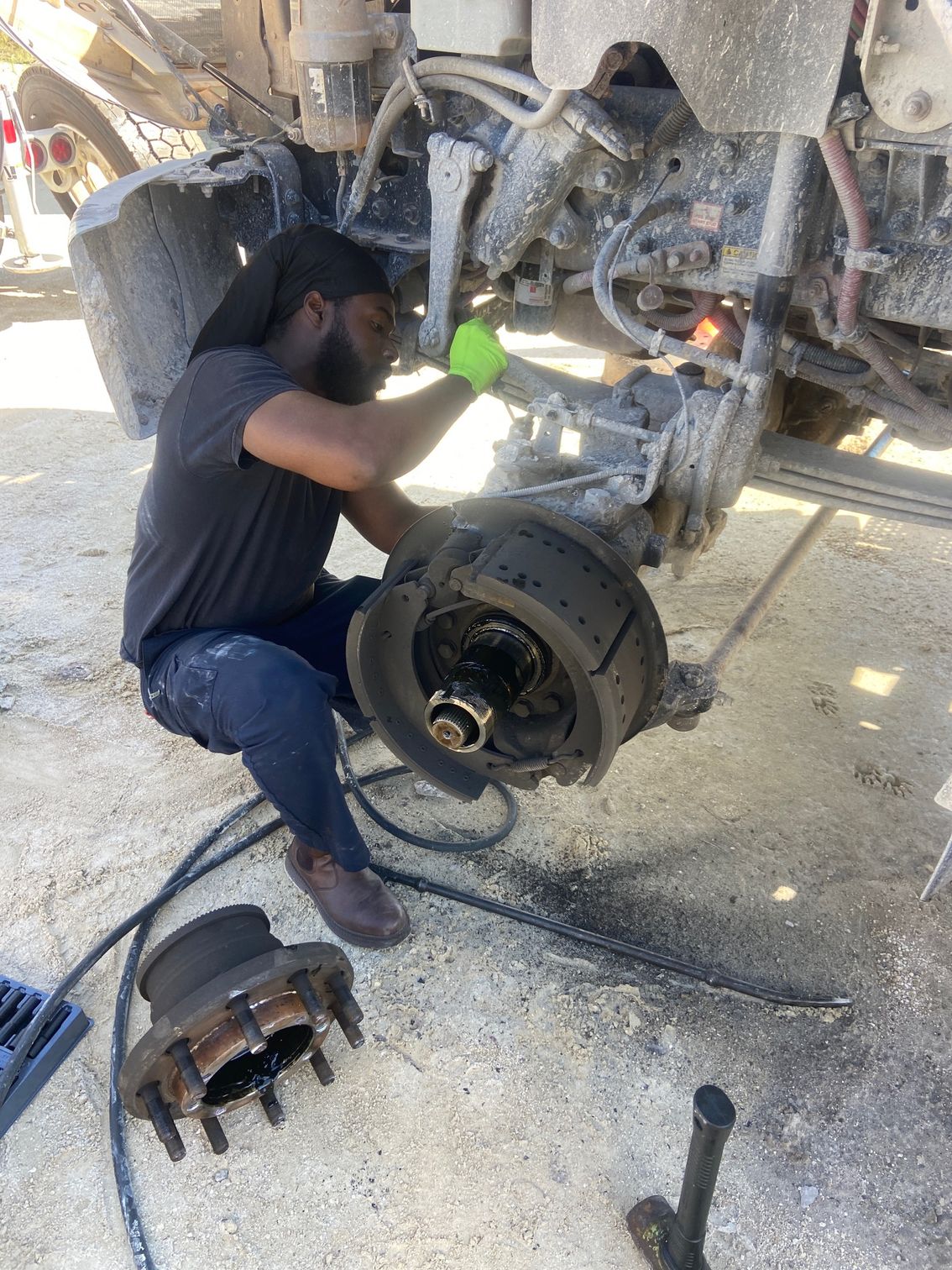 Mechanic in green gloves repairs truck wheel, outdoors, with tools.