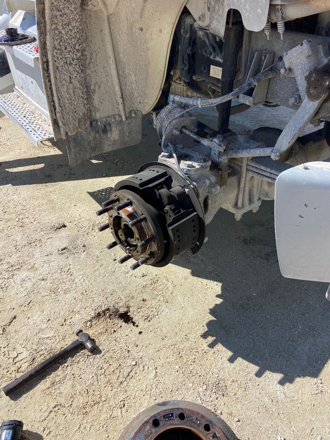 Truck wheel removed; tools on ground. Wheel hub exposed, covered in grease.